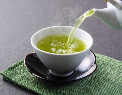 White teapot pouring green tea into a teacup.