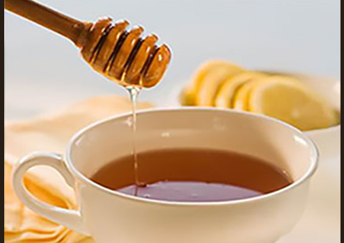 Cup of tea with a wooden honey stick dripping honey into the tea.